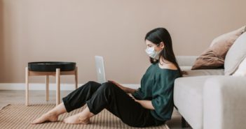 A girl looking at her computer while wearing a mask