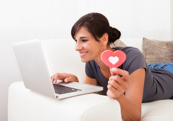 A woman using a laptop holding a heart