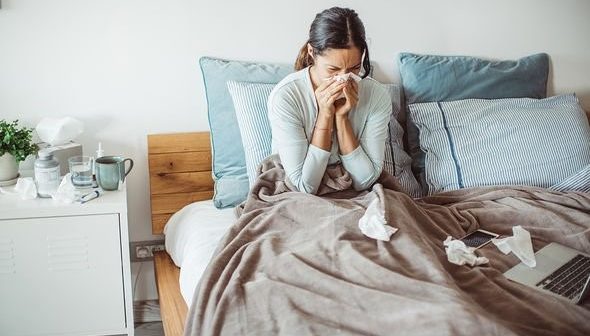 A woman blowing their nose on their bed