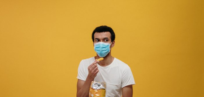 A man wearing a mask while trying to eat a Cheeto